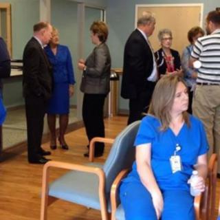 A group of people are engaged in conversation while a nurse in blue scrubs sits nearby.