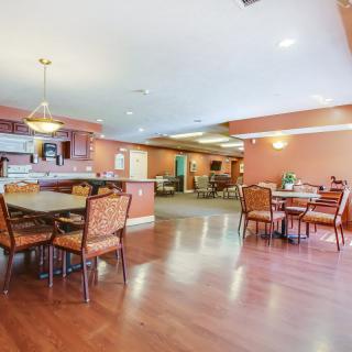 A spacious dining area with tables and chairs, featuring a warm color scheme and wooden flooring.