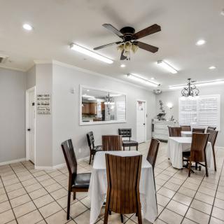 A cozy dining area with neatly arranged tables and chairs, featuring a ceiling fan and bright lighting.