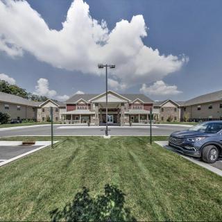 A wide view of a building with a parking lot and cars, set against a cloudy sky.