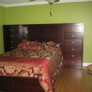 A bedroom with a large bed featuring an ornate headboard and built-in drawers against a green wall.