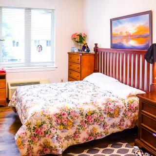 Cozy bedroom with a floral bedspread, wooden furniture, and a large window.