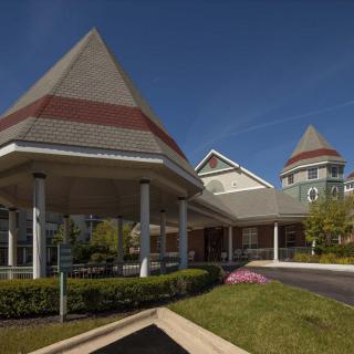 A scenic view of a building entrance with landscaped greenery and unique architectural features under a clear blue sky.