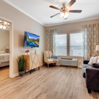 A modern living room with wood flooring and stylish decor, featuring a TV, armchair, sofa, and large windows with curtains.