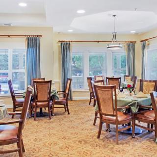 A bright dining room with elegant tables and chairs, surrounded by large windows and blue curtains.
