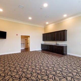 A spacious conference room with patterned carpeting, wall cabinets, and a mounted TV.