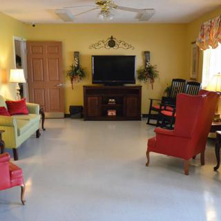 A cozy living room with yellow walls, featuring a television, a green sofa, and red accent chairs.
