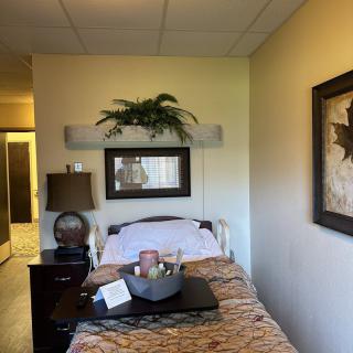 A hospital room with a neatly made bed, bedside table with a lamp, and decorative elements on the walls.