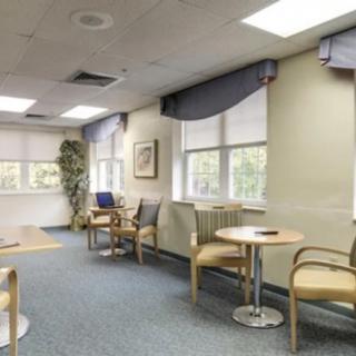 A brightly lit waiting room with chairs and tables arranged near large windows.