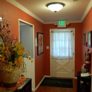 A warmly decorated hallway with artwork, flowers, and a door leading outside.