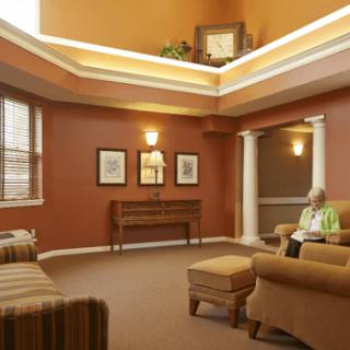A cozy lounge area with comfortable seating and warm lighting, featuring a senior individual sitting and reading.