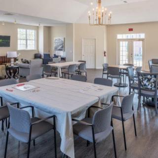 A spacious dining area with multiple tables and chairs, featuring a chandelier and hardwood floors.