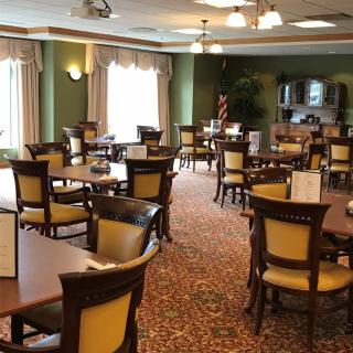 A well-lit dining area with neatly arranged tables and chairs, featuring elegant decor and carpeting.
