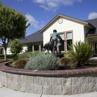 A statue of a person on horseback in front of a building surrounded by landscaped gardens.