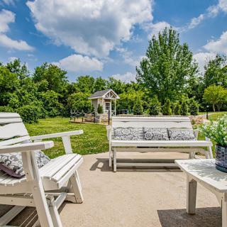 A sunny patio with white outdoor furniture overlooking a lush garden.