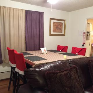A cozy dining room with a large table, surrounded by red chairs and accented with mismatched curtains.