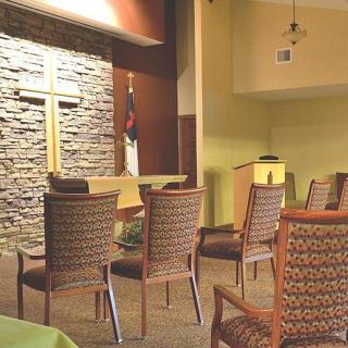 A serene chapel interior with a stone wall featuring a cross, accompanied by neatly arranged chairs and a pulpit.
