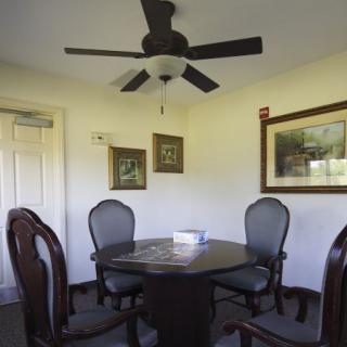 A cozy dining area with a round table, upholstered chairs, and a ceiling fan.