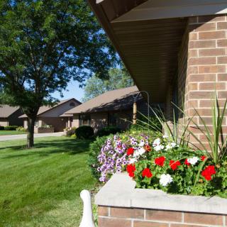 A suburban brick house with a colorful flower bed and a well-maintained green lawn on a sunny day.