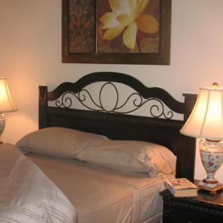 A cozy bedroom with a decorated headboard, two lamps on nightstands, and wall artwork.