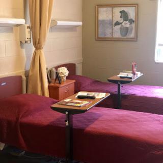 A patient room featuring two beds with side tables and a warm color scheme.