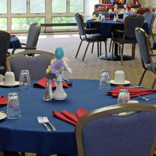 An indoor dining area set up with tables and chairs, featuring table settings with napkins, glasses, and centerpieces.