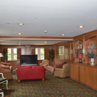 A cozy living room with wood paneling, featuring sofas, a television, and large windows.