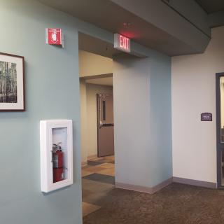 A hallway featuring a fire extinguisher, exit sign, and framed wall art.