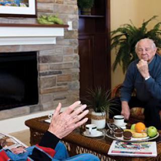 Two seniors engaged in conversation in a cozy living room setting.