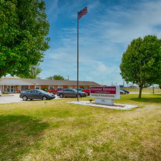 A school building with a parking lot, trees, and a flagpole on a sunny day.