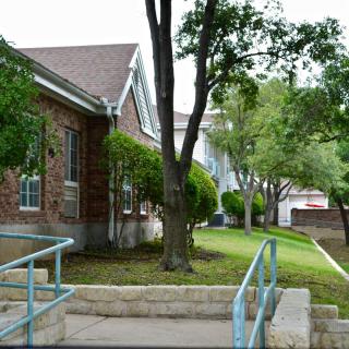 A brick building surrounded by trees and a sidewalk with an accessibility ramp.