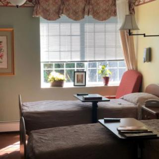 A hospital room with two beds and a bright window letting in sunlight.