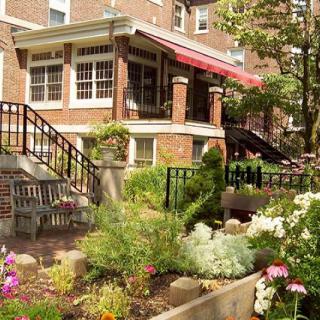 A lush garden with colorful flowers and outdoor seating in front of a charming brick building.