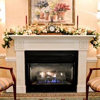 A cozy interior setting featuring a fireplace with floral decorations and chairs on either side.