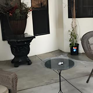 A cozy patio setup featuring a small glass table, comfortable chairs, and decorative plants.