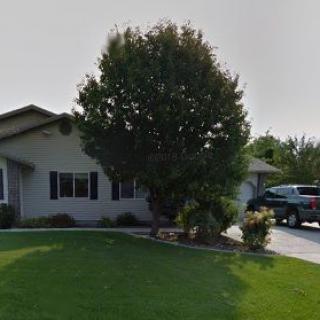 A suburban house with a large tree, well-maintained lawn, and a car parked in the driveway.