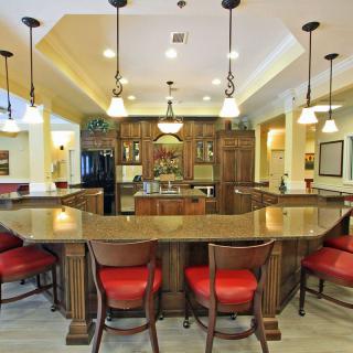 Spacious kitchen area with a central island, featuring red cushioned bar stools and elegant pendant lighting.