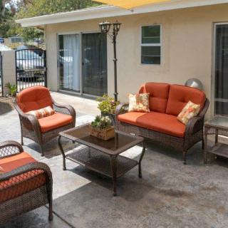 A cozy outdoor seating area with orange-cushioned chairs and sofa arranged around a glass-top table on the patio.