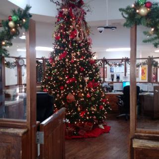 A beautifully decorated Christmas tree adorned with red and gold ornaments, set in a festive office environment.