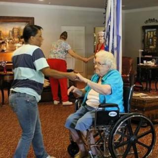 A caregiver interacts with an elderly person in a wheelchair at an assisted living facility.