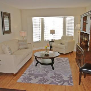 A cozy living room with a sofa, armchair, and coffee table centered on an area rug, illuminated by natural light from a large window.
