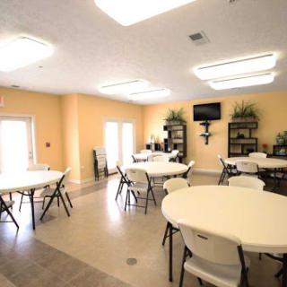 A spacious indoor meeting room featuring round tables, chairs, and warm-colored walls.