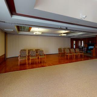 A spacious and empty waiting room featuring wooden chairs and a polished wood floor.