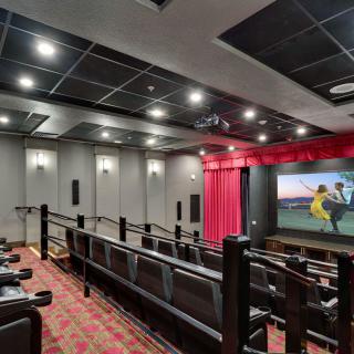 A cozy home theater with tiered seating and a large screen, featuring red curtains and a carpeted floor.