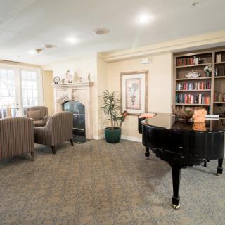 A cozy living room featuring a grand piano, bookshelf, and fireplace.