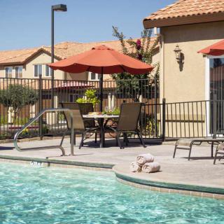 A sunny day by the swimming pool with patio furniture and umbrellas in a residential area.