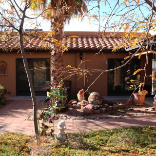A sunny courtyard with a garden in front of a house featuring a terracotta roof.