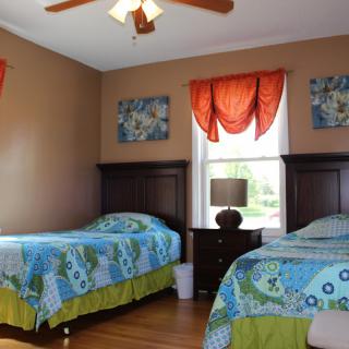 A cozy bedroom with two twin beds, vibrant bedding, and a warm color scheme featuring orange curtains and artwork.