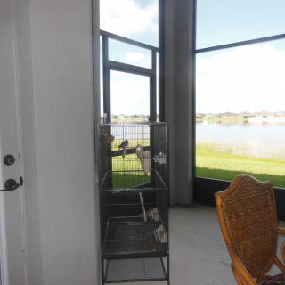 A room with a bird cage and a view of a lake through glass doors.