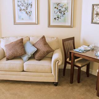 A cozy living room with a beige sofa adorned with cushions, accompanied by wall art and a small dining table.